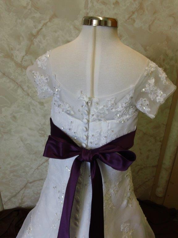 White lace flower girl gown with a purple sash.