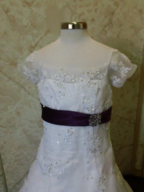 White lace flower girl gown with a purple sash.