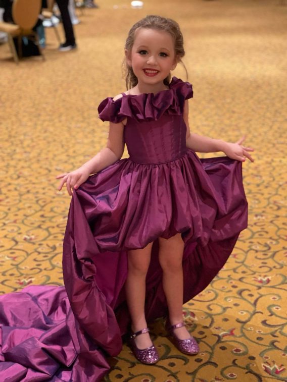 Little pageant queen wearing an original high low purple dress.