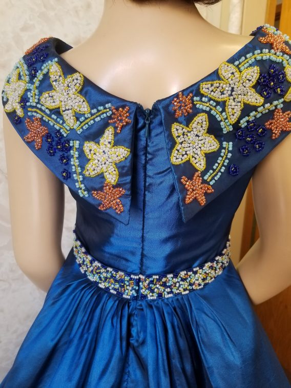 Girls long blue pageant dress embellished with an extravagant beaded cowl collar, and waistline. The beading details remind us of a seaside beach pageant.
