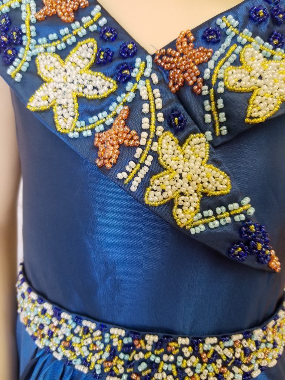 Girls long blue pageant dress embellished with an extravagant beaded cowl collar, and waistline. The beading details remind us of a seaside beach pageant.